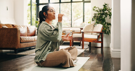 Fototapeta premium Yoga, woman and drinking water in living room with bottle, fitness and hydration break for wellness. Flare, mature person and liquid beverage in home lounge with exercise rest, thirst and self care.
