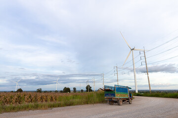 A heavy transport truck travels along a rural highway through a summer landscape of green farm fields and agriculture equipment under a clear blue sky