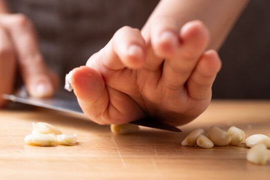 Close up of hand crushing fresh garlic clove with a knife on a wooden cutting board, prepared for cooking