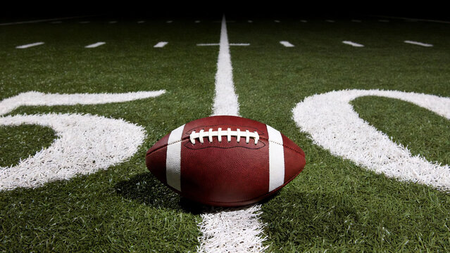 American Football Ball on 50 Yard Line Under Stadium Lights &ndash; Professional Sports Field Background with Copy Space