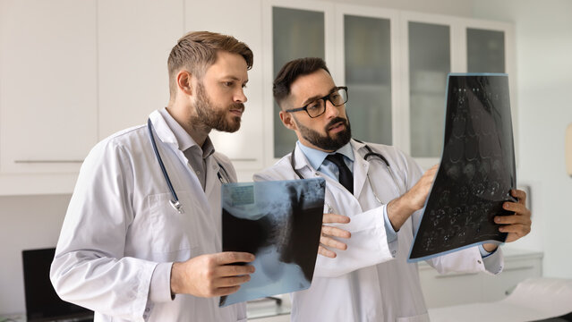 Difficult case discussion. Two young male physicians surgeons oncologists focused on patient radiographs talk compare results to solve challenging diagnosis analyze symptoms select correct treatment