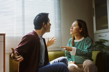 Young couple having a serious argument at home, expressing anger and disagreement, experiencing...