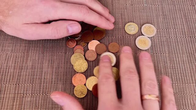 A high-angle close-up shot of a person's hands sorting and counting a variety of Euro coins, including cents and two-euro pieces.