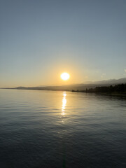 Obraz premium Scenic sunset over Issyk Kul Lake in Kyrgyzstan. The sun sets behind the mountains, casting a golden reflection across the water.