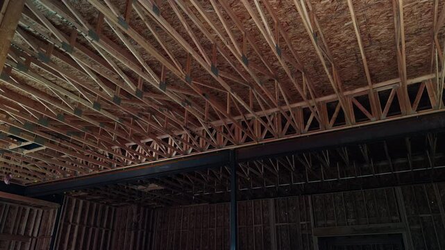 Slow steady pan of exposed wooden roof trusses and central steel beam inside unfinished structure.
