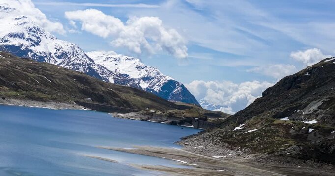 Montespluga lake shoreline next to a rocky mountain with snow capped peaks in the background. Aerial Hyperlapse