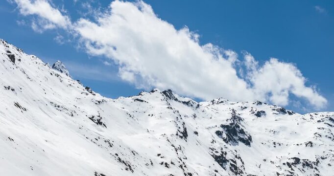 Snow covering jagged mountain peaks in the Italian Alps under a blue sky with white clouds. Aerial,Hyperlapse