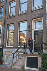 Woman standing on the steps of a traditional canal house in amsterdam. Enjoying a travel vacation in europe. Reflecting a sense of adventure. Relaxation. And cultural exploration in the historic city