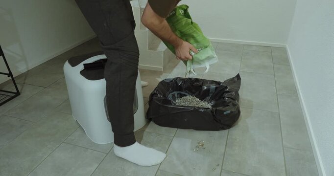 Man preparing and cleaning a cat litter box indoors, pouring fresh litter into a lined container. Concept of pet care, hygiene routine, household maintenance, and responsible pet ownership.