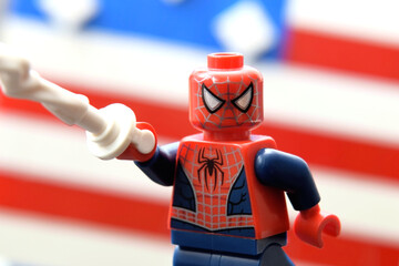 Fototapeta premium Lego minifigure of Spiderman in costume with web in a hand against an American stripped flag. Editorial illustrative image of popular children toys.