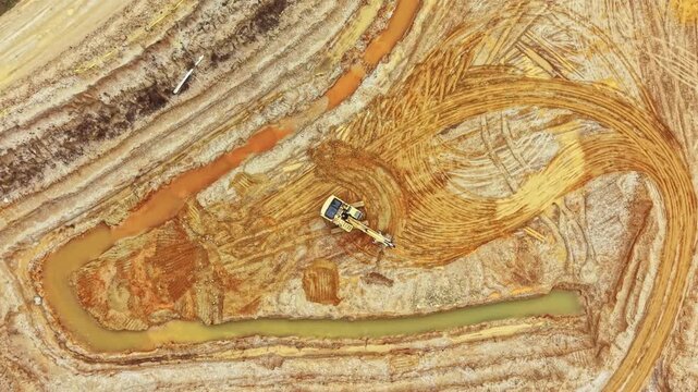 Heavy machinery is working to move soil and reshape the landscape in a large construction site near a water body. The site shows distinct patterns in the earth.