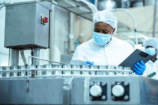 Manufacturing supervisor checks batch of canned food products on assembly line while following safety protocol in processing plant, representing industrial efficiency and compliance control.