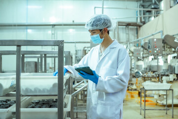 Naklejka premium Quality control employee monitors production status using digital device in automated food processing environment, ensuring traceability and regulatory compliance procedures.