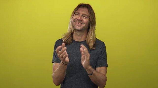 Blond man smiling and clapping hands in a vibrant yellow studio; support appreciation celebration approval.