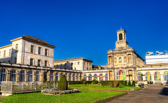Scenic sunny view of the historic stone architecture, chapel clock tower, and green courtyard of the Lariboisiere Hospital in Paris, France.