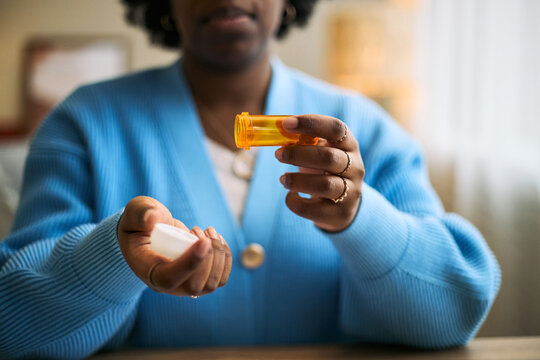 Middle aged Black woman holding prescription pill bottle and pouring medication into hand, focusing on healthcare and femtech solutions for womens health management at home
