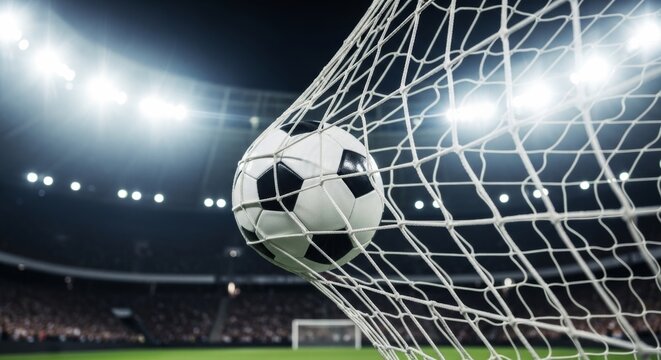 Soccer ball hitting the back of the net in a large floodlit stadium at night, capturing the moment of a winning goal during a professional match.