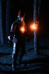 Obraz premium A knight in full armor, sword and torch in hand, walks through a gloomy night forest. A medieval warrior, bloodied and scarred, hunts and searches in the darkness.