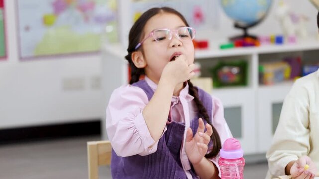 Young Asian Girl Wearing Pink Glasses Eating Lunch in Classroom