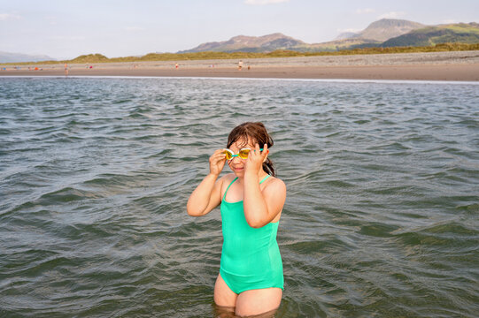 Child adjusting swimming goggles while standing in sea water.