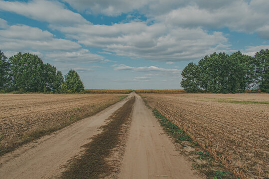 Panorama of a road between a farm field against a sky background.