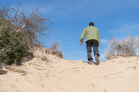 Man hiking up sand dune reaching for summit