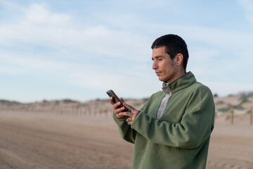Young man using smartphone on sandy beach