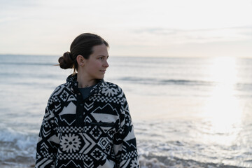 Woman contemplating ocean sunset wearing fleece sweater on beach © Cavan