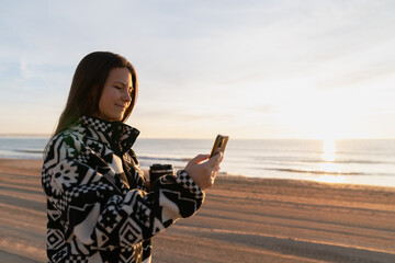 Woman using smartphone holding travel mug on beach © Cavan