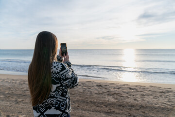 Woman capturing sunrise ocean view with smartphone