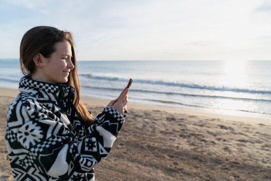 Young woman taking ocean picture with phone on beach