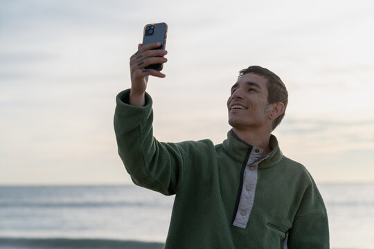 Young man smiling taking selfie by ocean