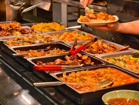 Chef serves delicious hot food selection from a fully stocked Asian buffet line with various options.
