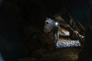 Woman exploring dark cave with headlamp illuminating path