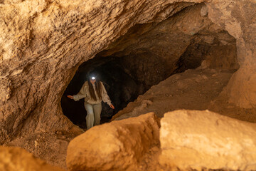 Woman exploring dark cave with headlamp for adventure