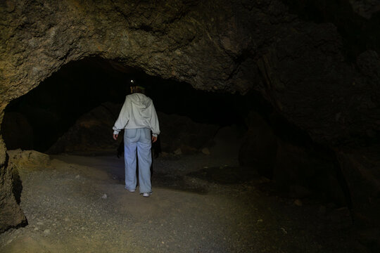 Person exploring dark underground cave with headlamp light