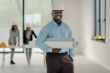 African american engineer holding blueprints smiling at construction site
