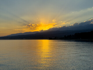 Obraz premium Scenic sunset over Issyk Kul Lake in Kyrgyzstan. The sun sets behind the mountains, casting a golden reflection across the water.