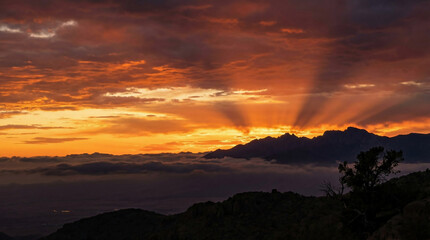Obraz premium Dramatic sunset with radiant crepuscular sun rays over silhouetted mountains and clouds