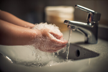 Fototapeta premium Person washing hands thoroughly with soap bubbles under running water from modern faucet in bathroom sink for hygiene and cleanliness practice