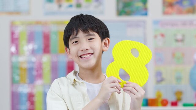 Smiling Schoolboy Holding Foam Number Eight in Classroom