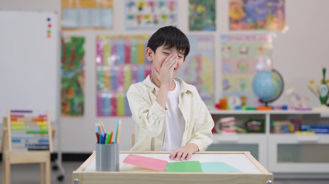 Shy Schoolboy Covering Face at Classroom Desk