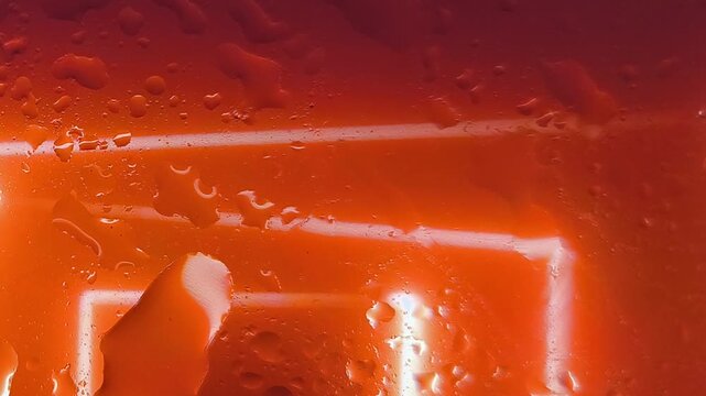Close-up of a finger touching a glowing orange screen with water droplets and a neon-like square outline.