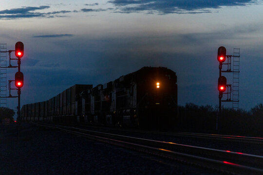 Freight train approaches red signals in blue hour light