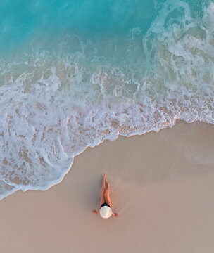 Aerial view of woman on sandy beach as ocean waves roll in.