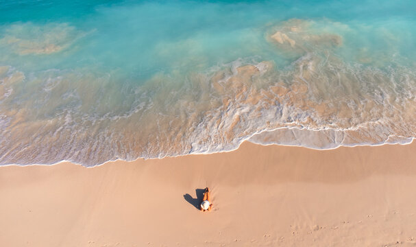 Aerial view of woman on sandy beach as ocean waves roll in.