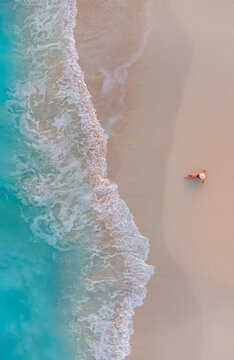 Aerial view of woman on sandy beach as ocean waves roll in.