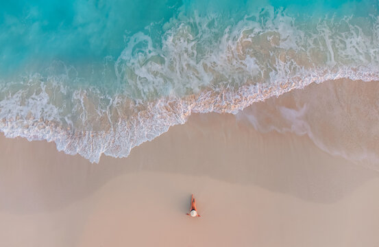 Aerial view of woman on sandy beach as ocean waves roll in.