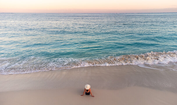 Aerial view of woman on sandy beach near turquoise ocean waters.