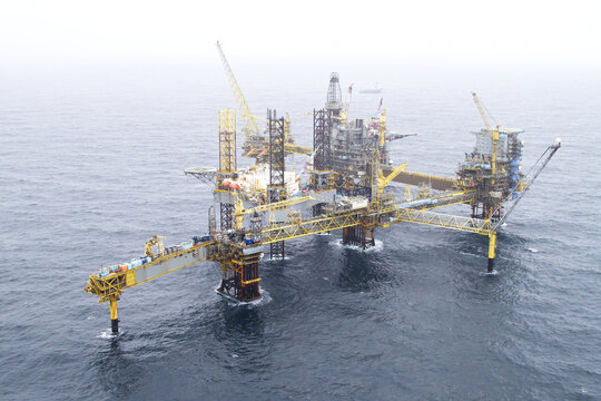 Esbjerg, Denmark - 13 February 2026: Aerial view of a massive offshore oil rig standing tall amidst the vast, grey expanse of the sea, its yellow structures cutting through the muted tones of the sky.